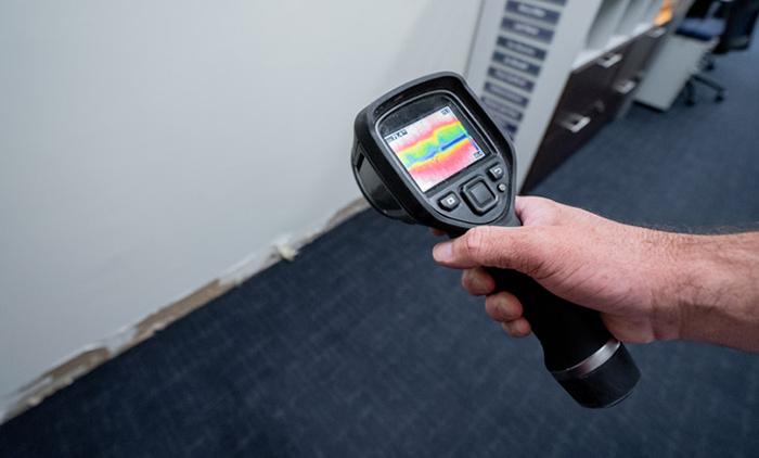 A plumber inspecting a wall with specialized leak detection equipment, highlighting signs of hidden leaks like damp spots and water stains. The image represents the expertise of Water Heater Repair McKinney, TX in identifying and resolving hidden plumbing issues. 